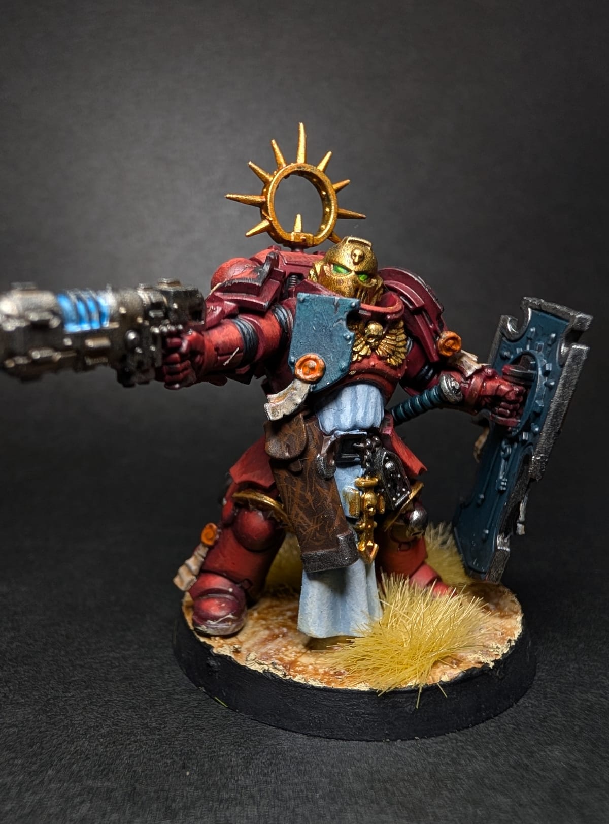 Blood Angels Lieutenant in red armour with a gold halo, a relic shield and a plasma pistol, on a sandy base