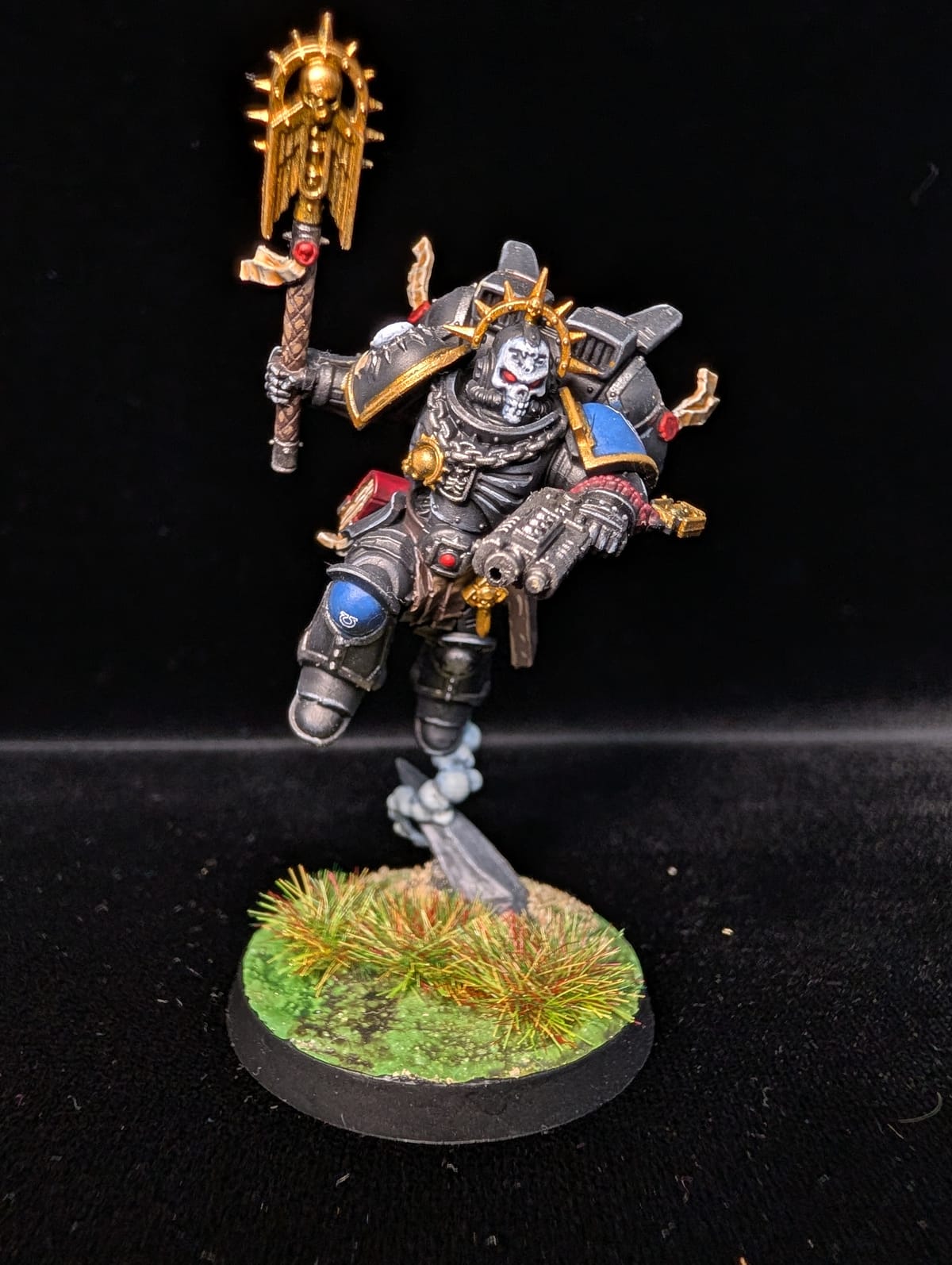 Space Marine Chaplain in black armour with a skull helm and crozius, mid-leap on a grassy base
