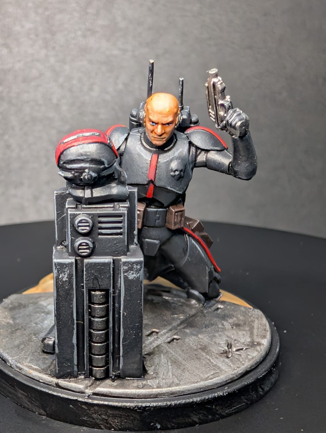 Star Wars Shatterpoint Tech miniature in dark armour with red goggles, crouched behind a crate on a metal deck base